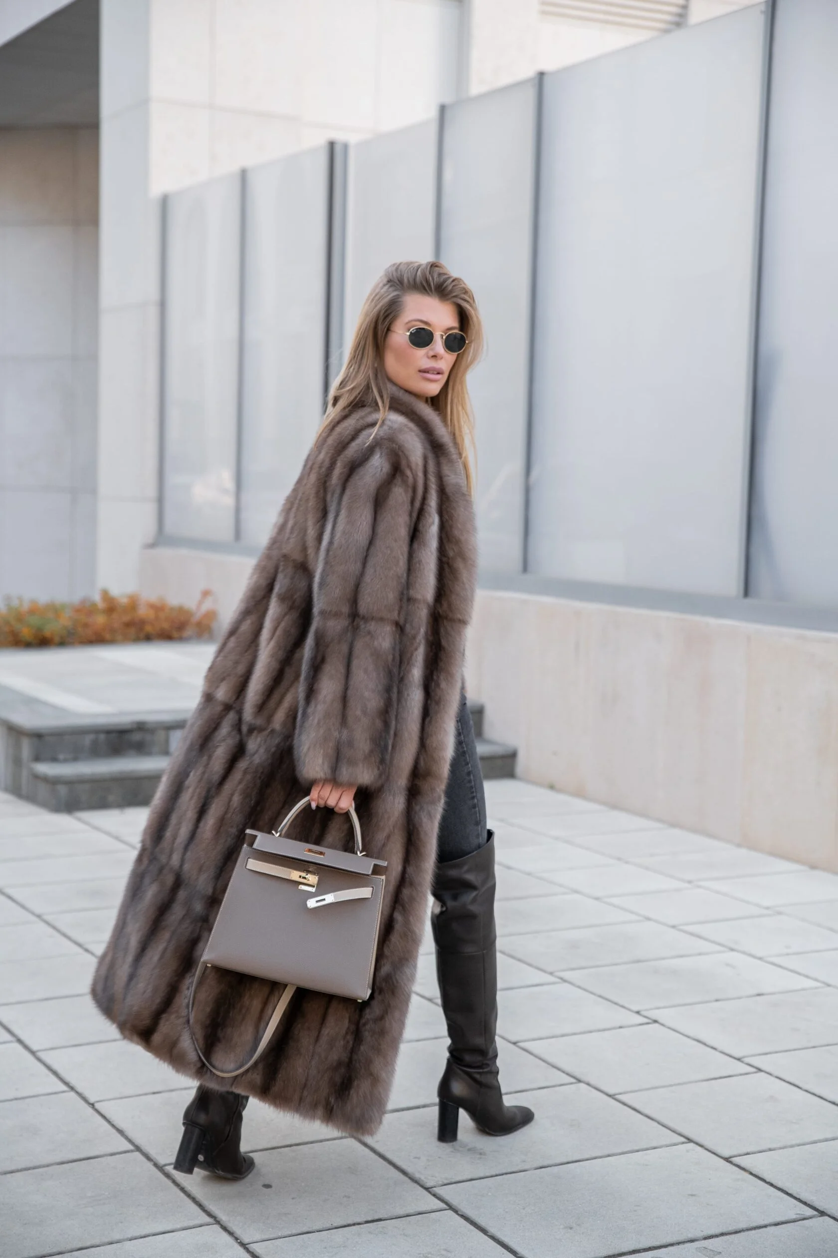Женщина в длинной роскошной меховой шубе идет по городской улице,